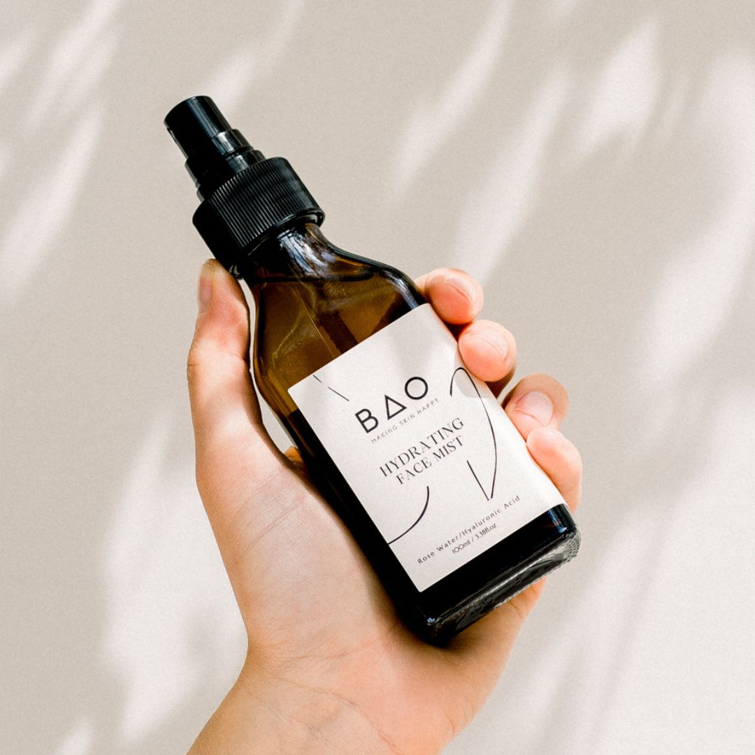 A hand holding a brown bottle with a white spray nozzle labeled &