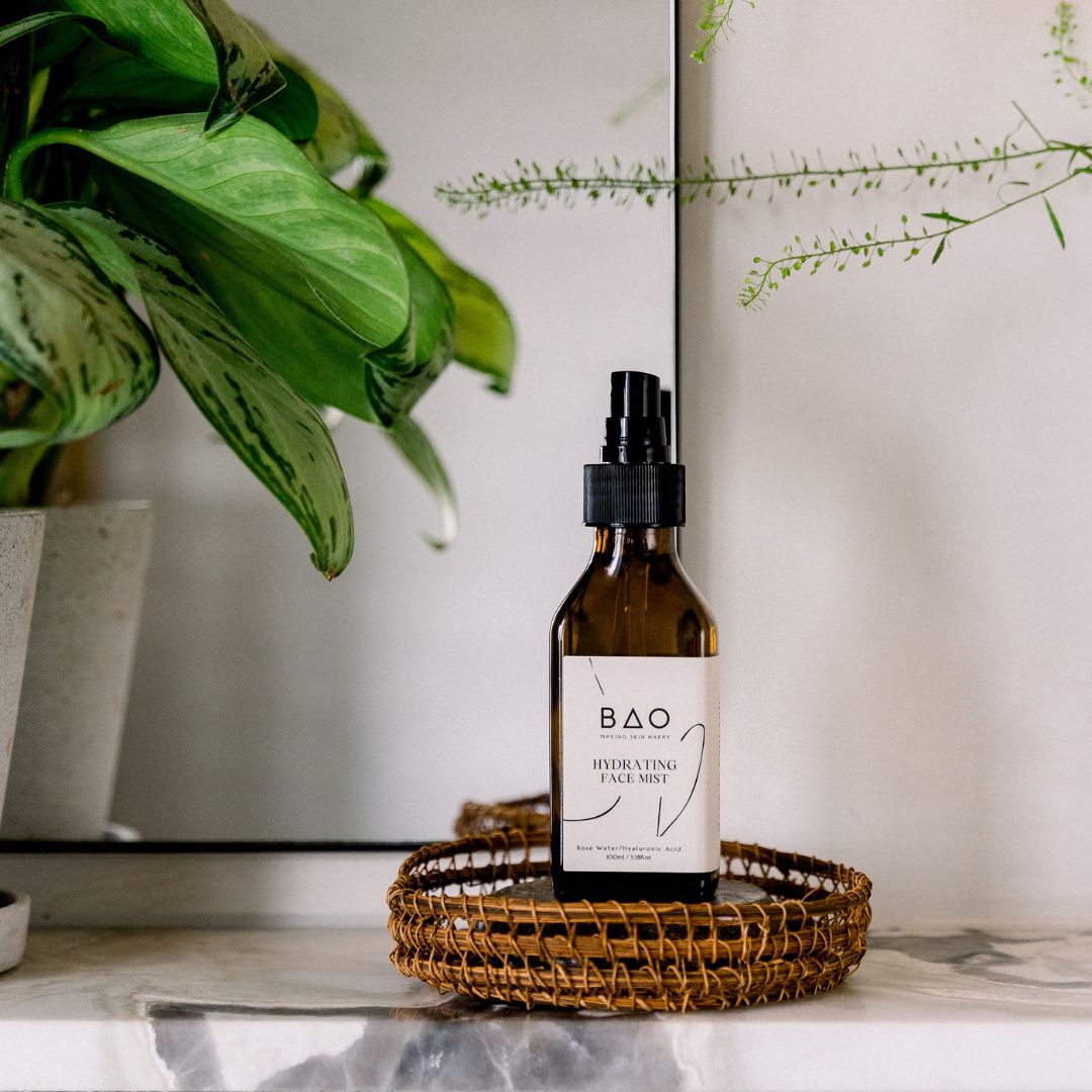 BAO Hydrating Face Mist bottle on a woven tray beside a bathroom mirror and plant