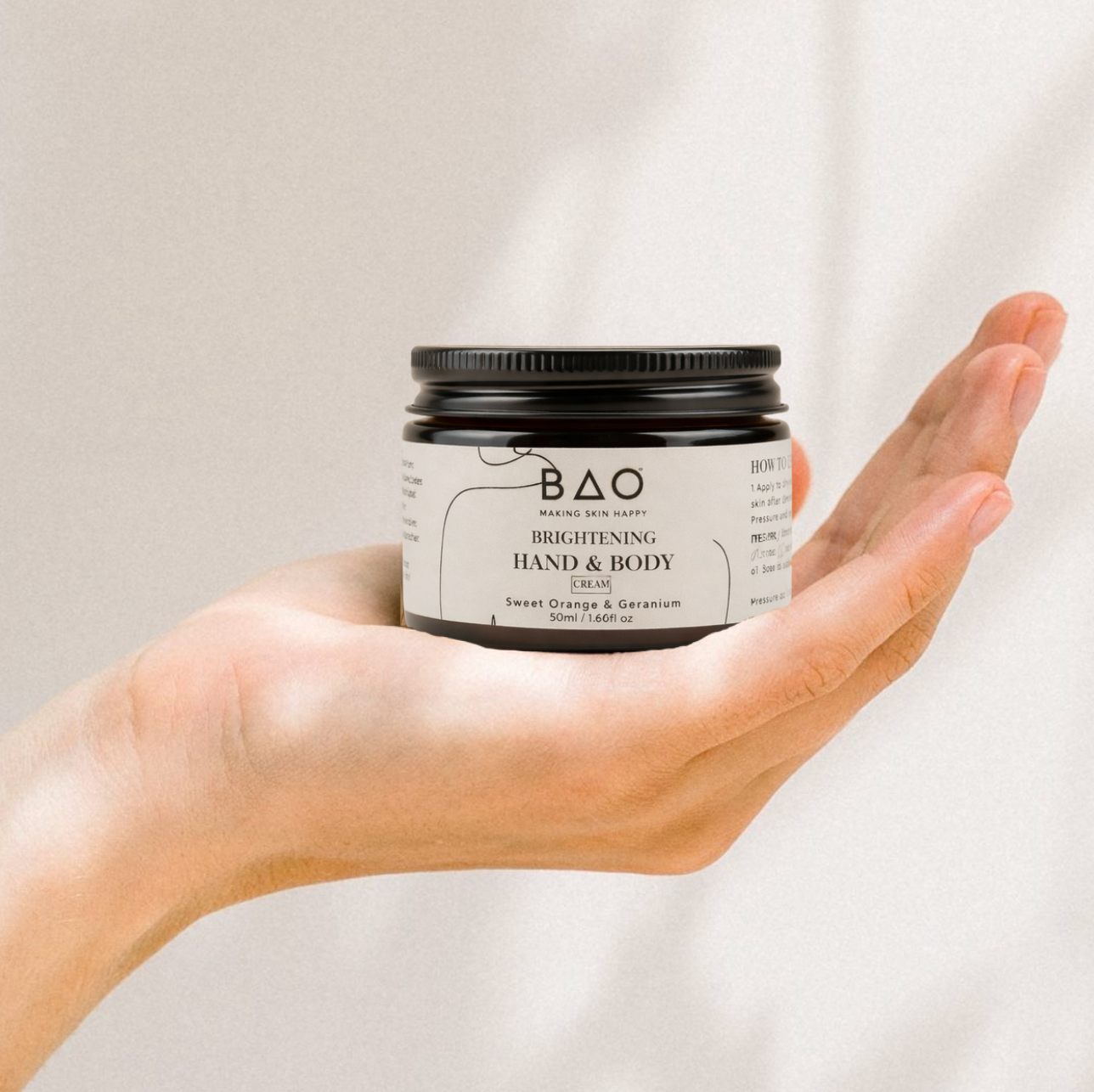 Hand holding a jar of BAO Brightening Hand & Body Cream against a plain background
