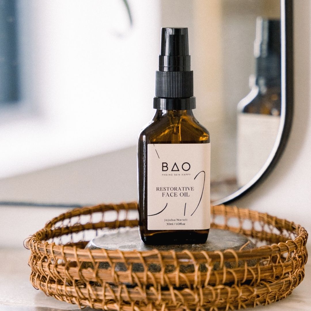 Bottle of BAO Restorative Face Oil on a woven tray with a mirror in the background