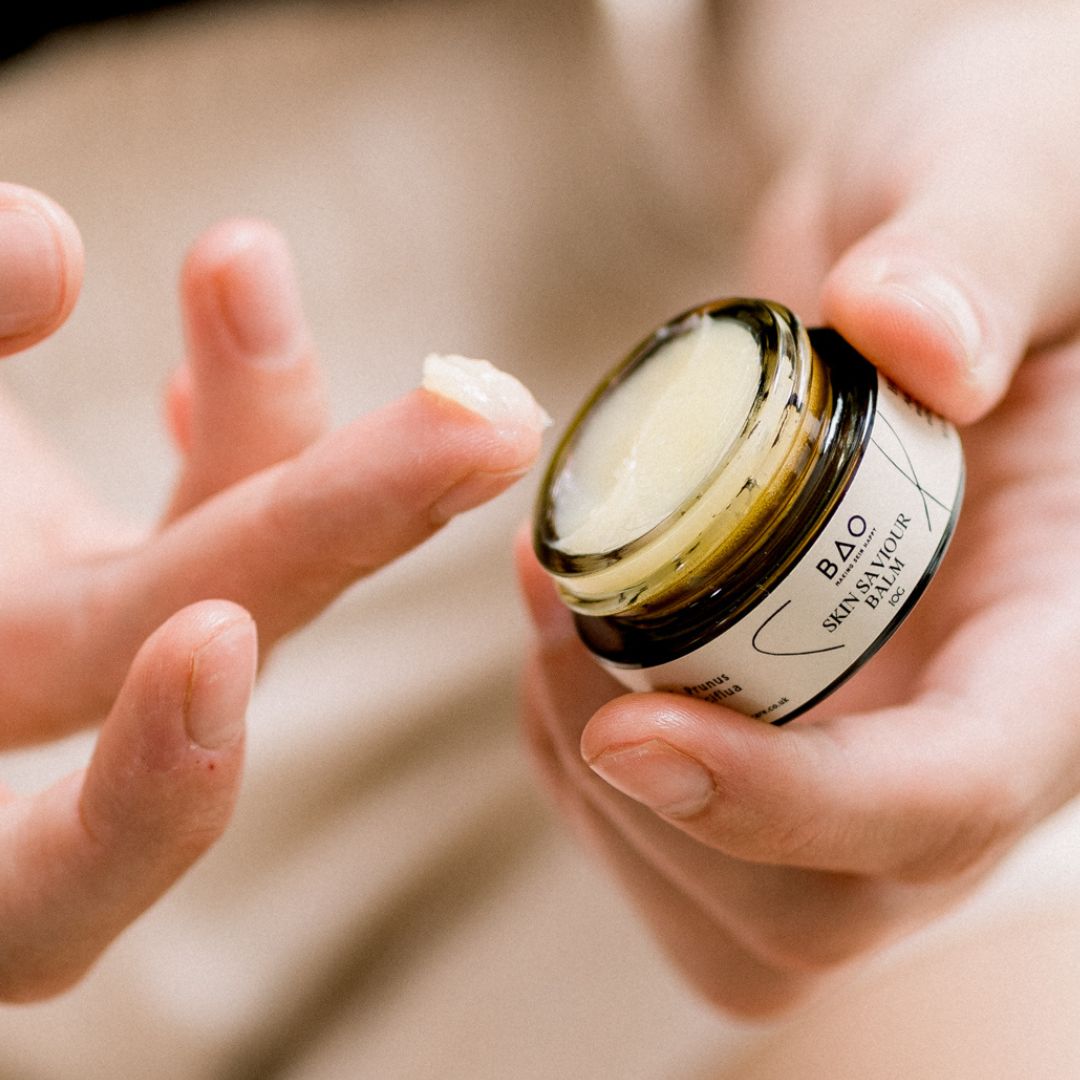 Hand scooping BAO Skin Saviour Balm from an open jar with a fingertip