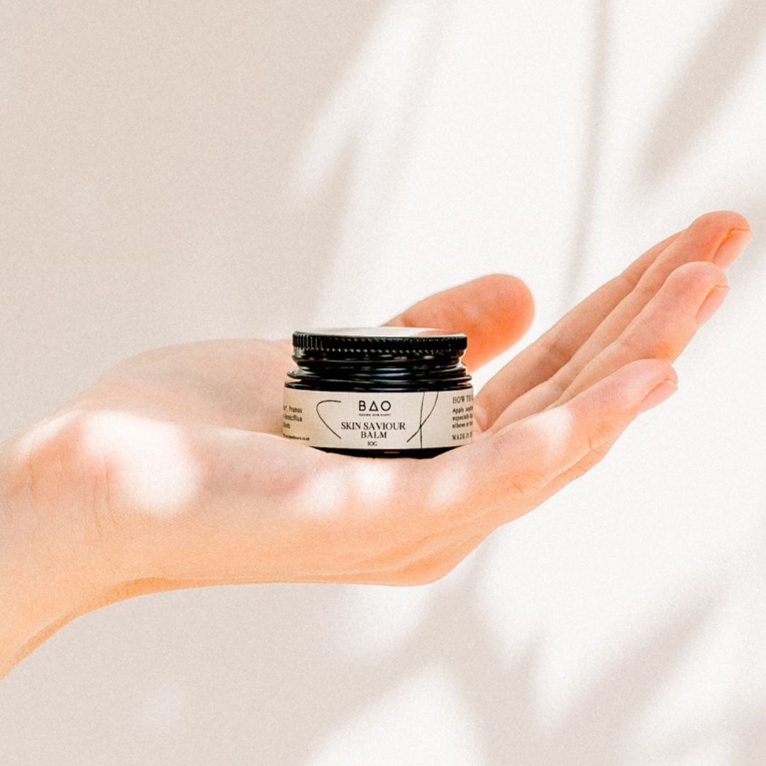BAO Skin Saviour Balm jar held open-palm against a sunlit backdrop