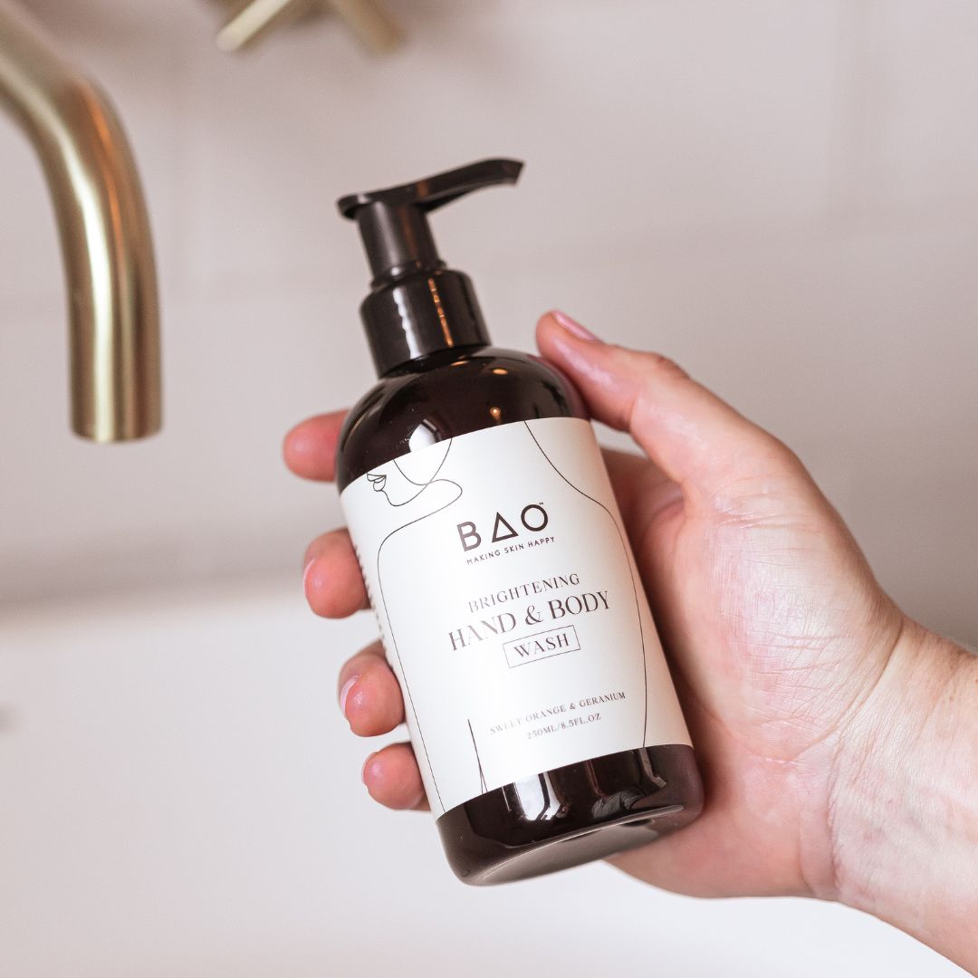 Hand holding the BAO Brightening Hand & Body Wash bottle beside a bathroom tap