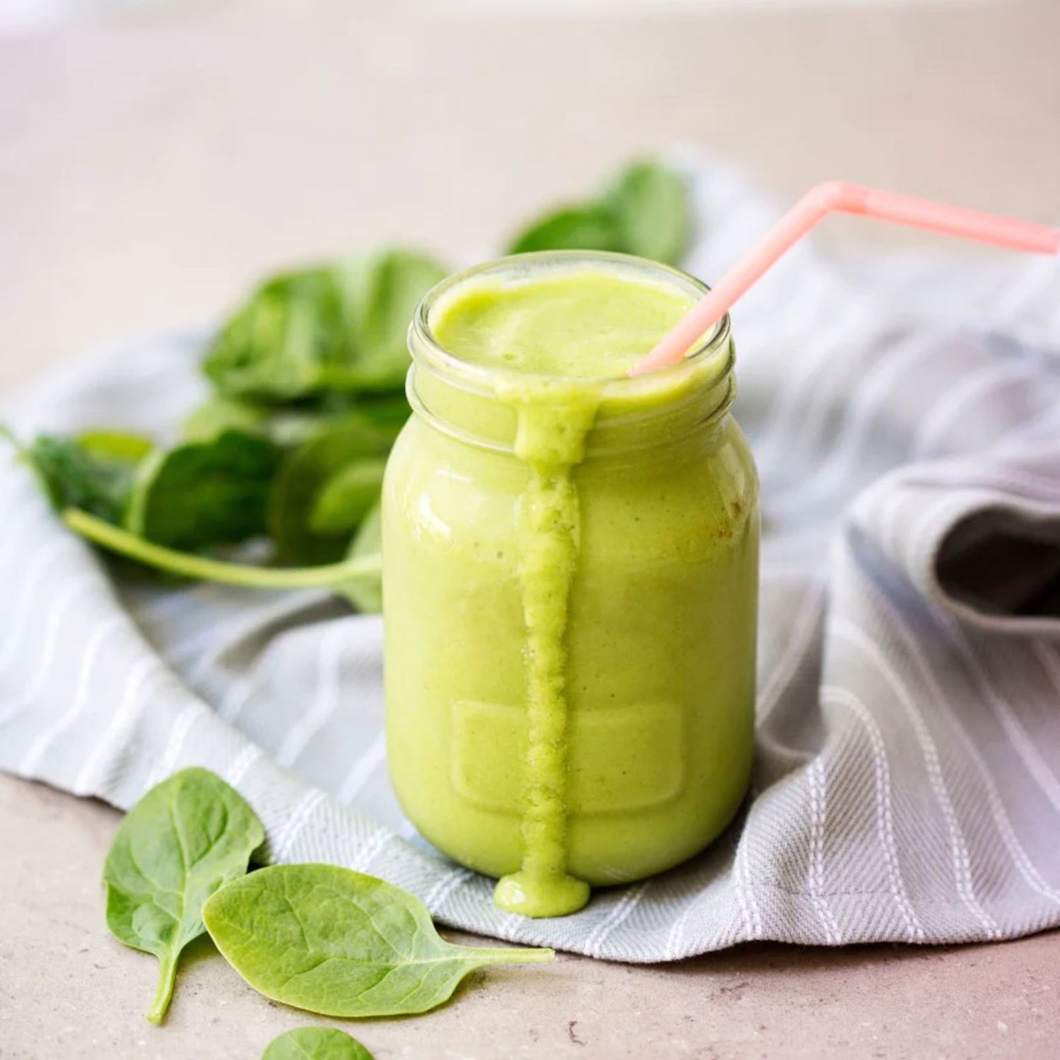 Green smoothie in a recyclable glass with spinach on a table.