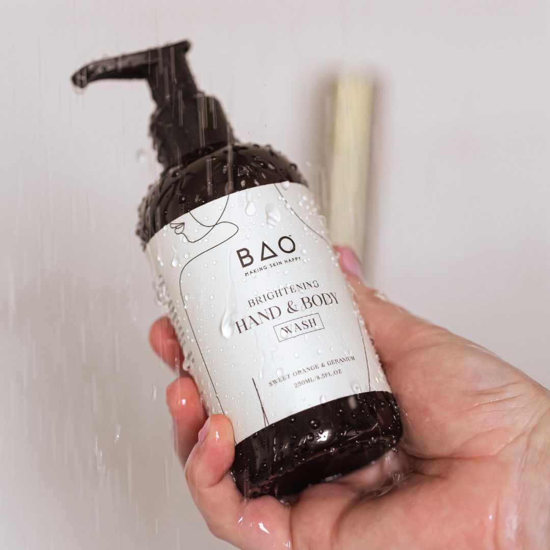 Hand holding BAO Brightening Hand & Body Wash bottle under running shower water