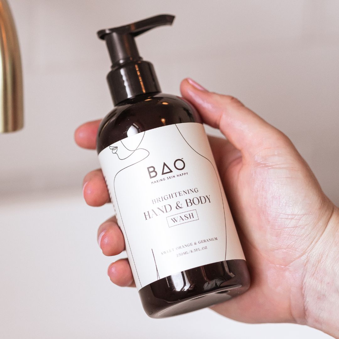 Hand holding BAO Brightening Hand & Body Wash bottle beside a bathroom tap