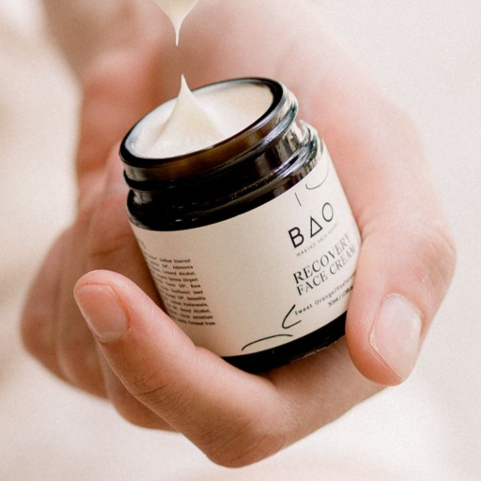 Hand holding a jar of BAO Recovery Face Cream with cream being squeezed out.