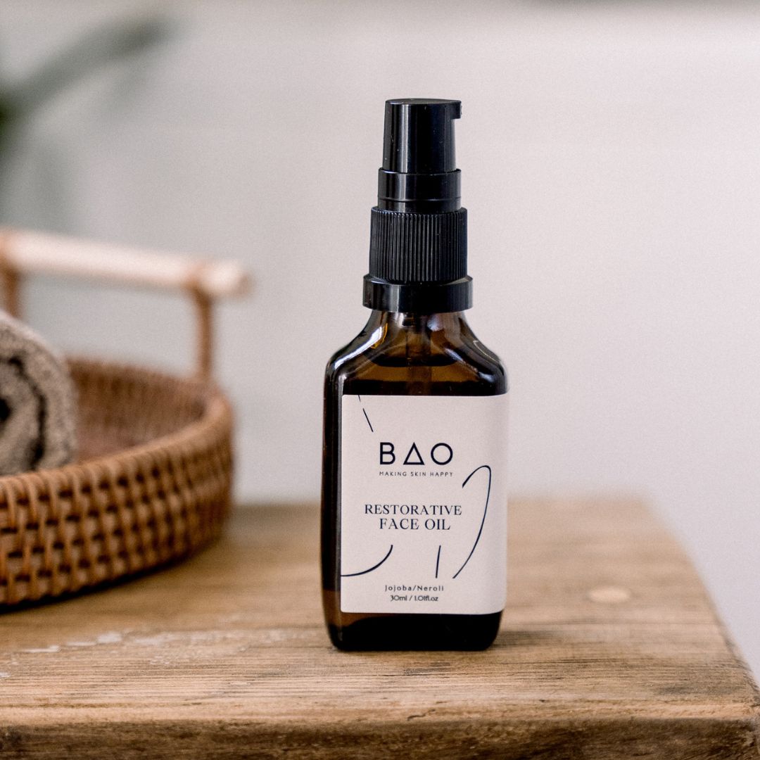 BAO Restorative Face Oil bottle standing on a wooden table beside a woven basket