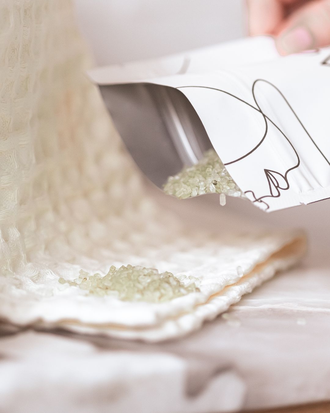 Hand pouring BAO Healing Bath Salts from the pouch onto a folded towel