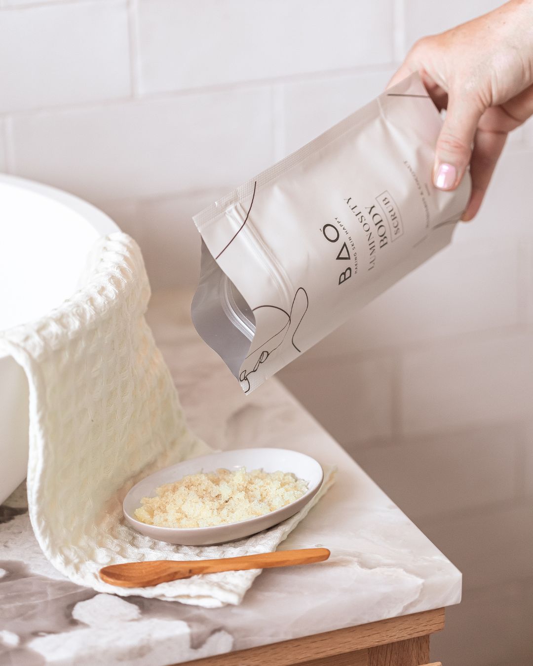 Hand pouring BAO Luminosity Body Scrub from the pouch into a bowl