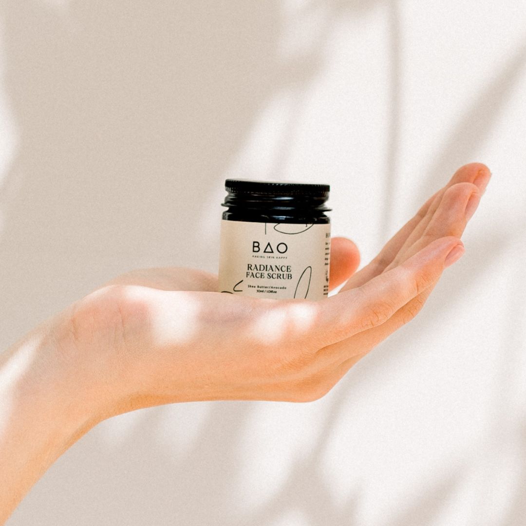 BAO Radiance Face Scrub jar held open-palm against a sunlit backdrop