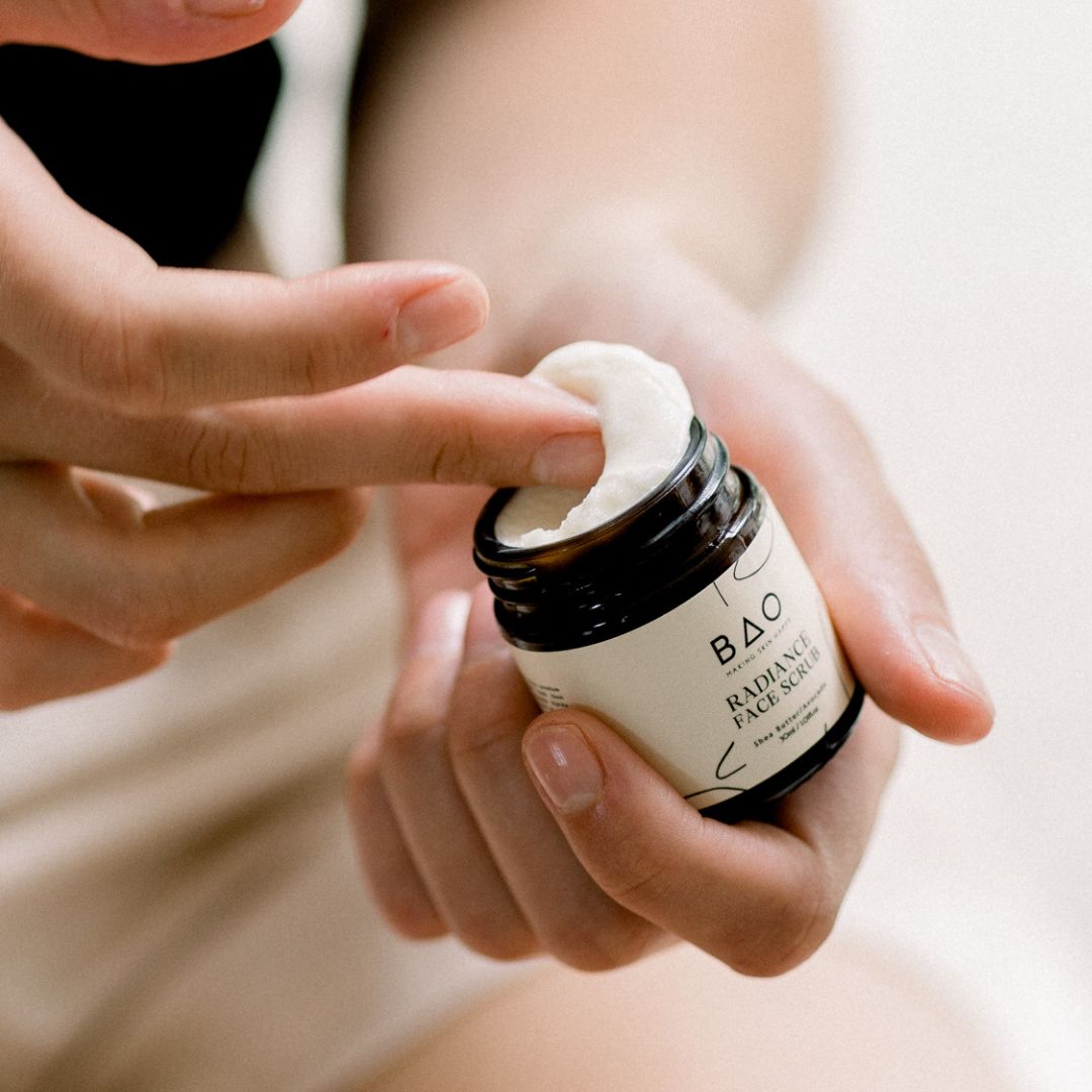 Fingers dipping into an open jar of BAO Radiance Face Scrub to scoop out the product
