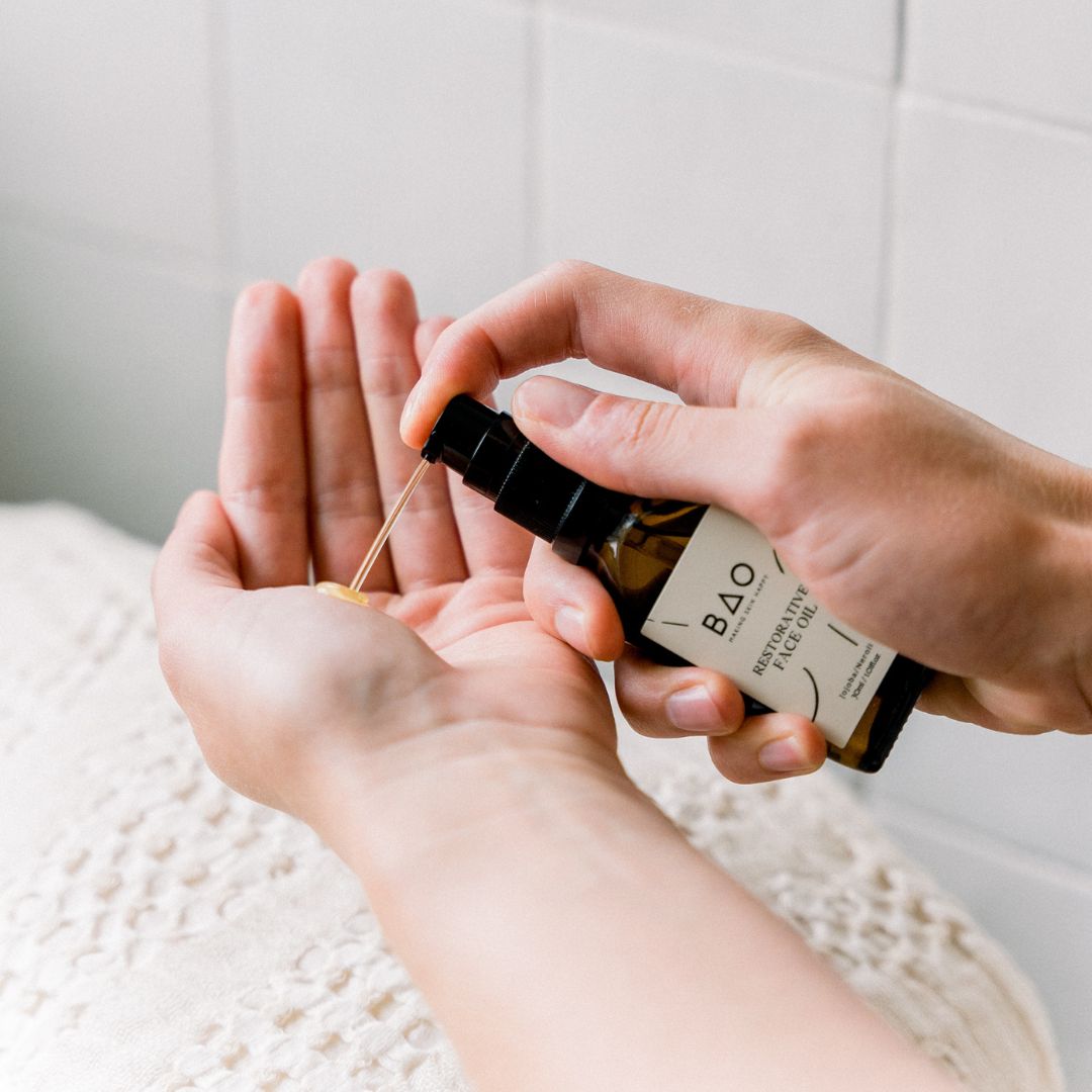 Dropper from a BAO Restorative Face Oil bottle releasing a drop of oil onto an open palm