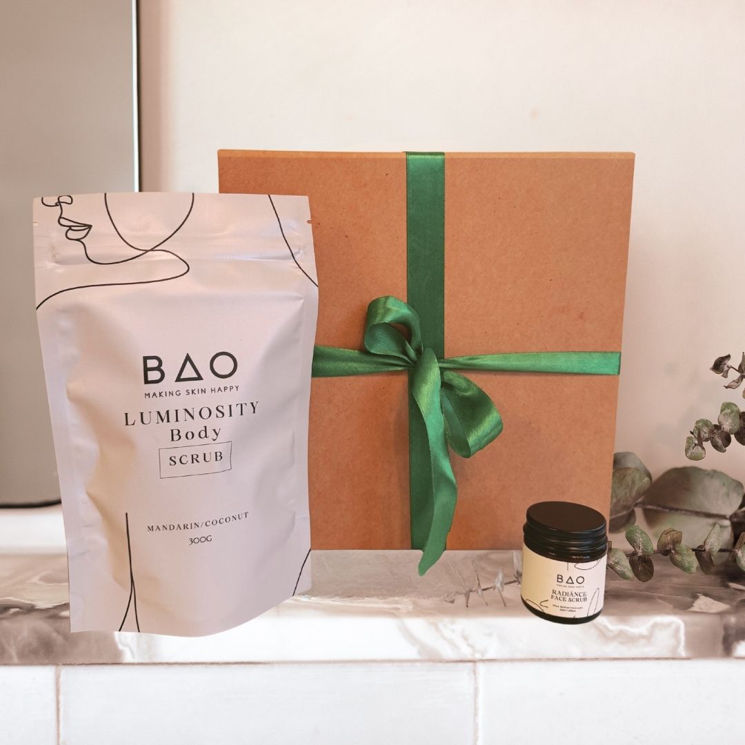 BAO Luminosity Body Scrub packaging with a brown gift box and green ribbon on a white surface.