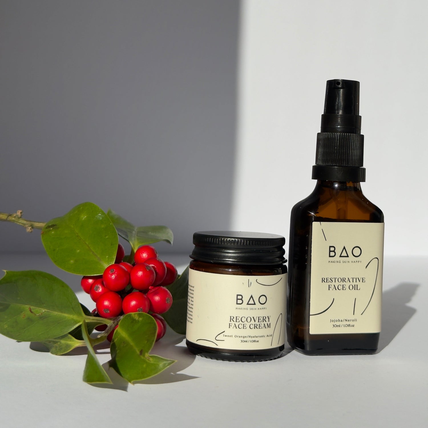 Two bottles of BAO skincare product on a white surface with a plant and berries in the background.