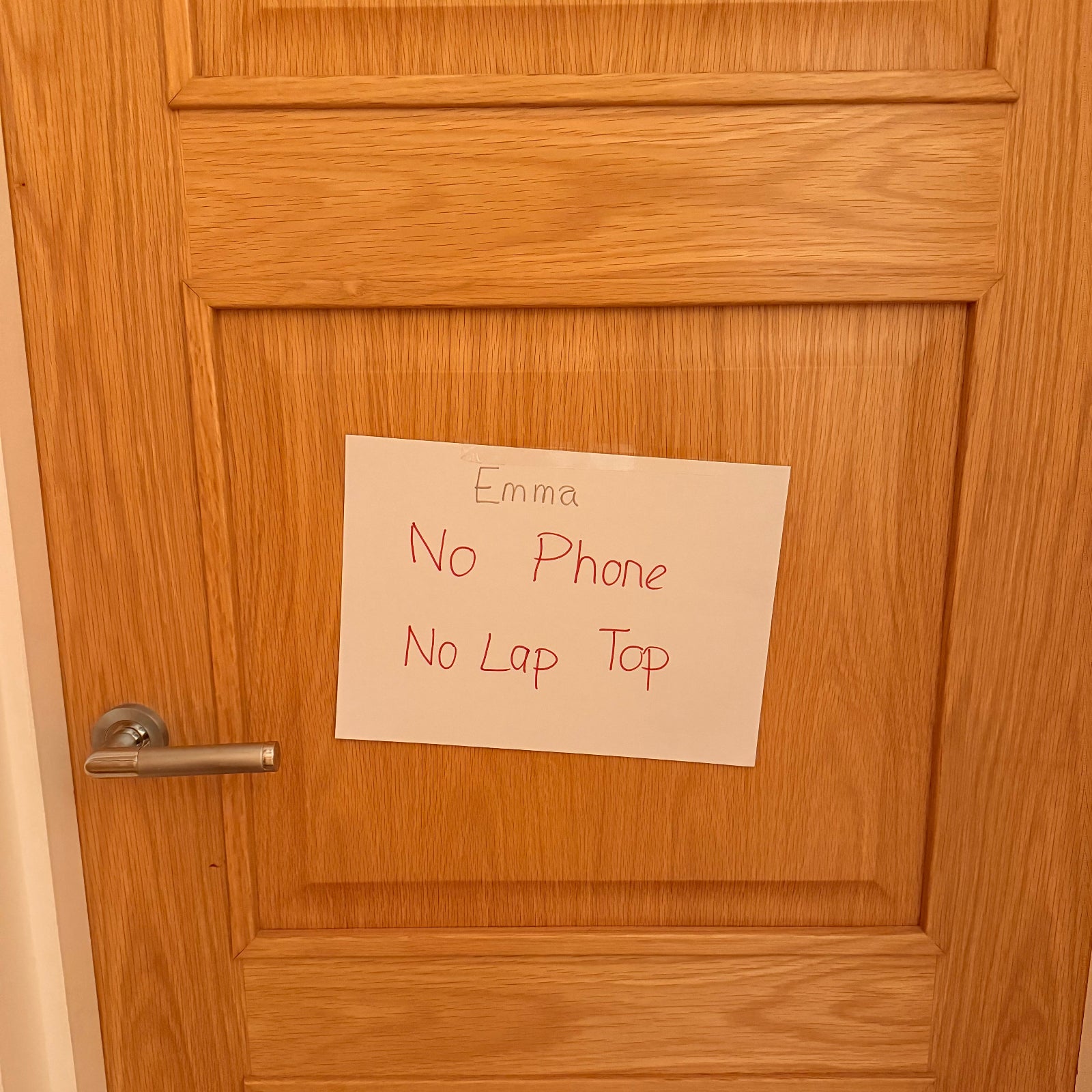 Wooden door with a sign reading 'No Phone, No Lap Top' attached to it.