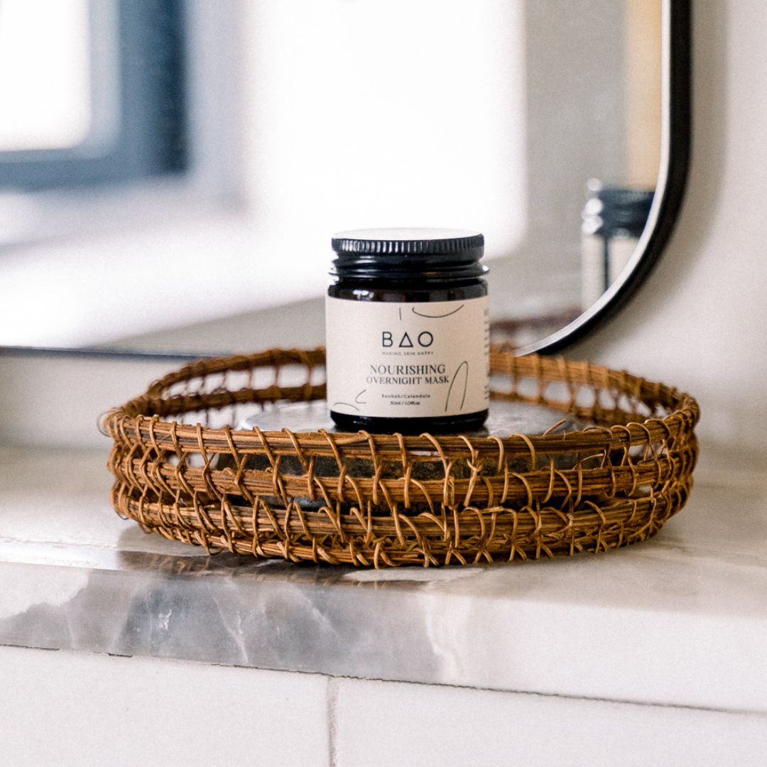BAO Nourishing Overnight Mask jar on a woven tray beside a bathroom mirror