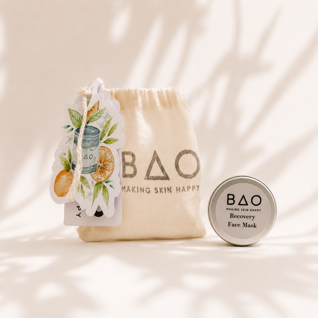 BAO Recovery Face Mask trial set displayed in a soft editorial skincare scene with a natural cotton BAO pouch, illustrated botanical tag and silver sample tin against a warm neutral background with delicate shadowing