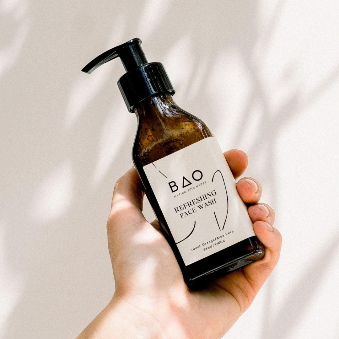 Hand holding BAO Refreshing Face Wash bottle against a sunlit wall with leaf shadows