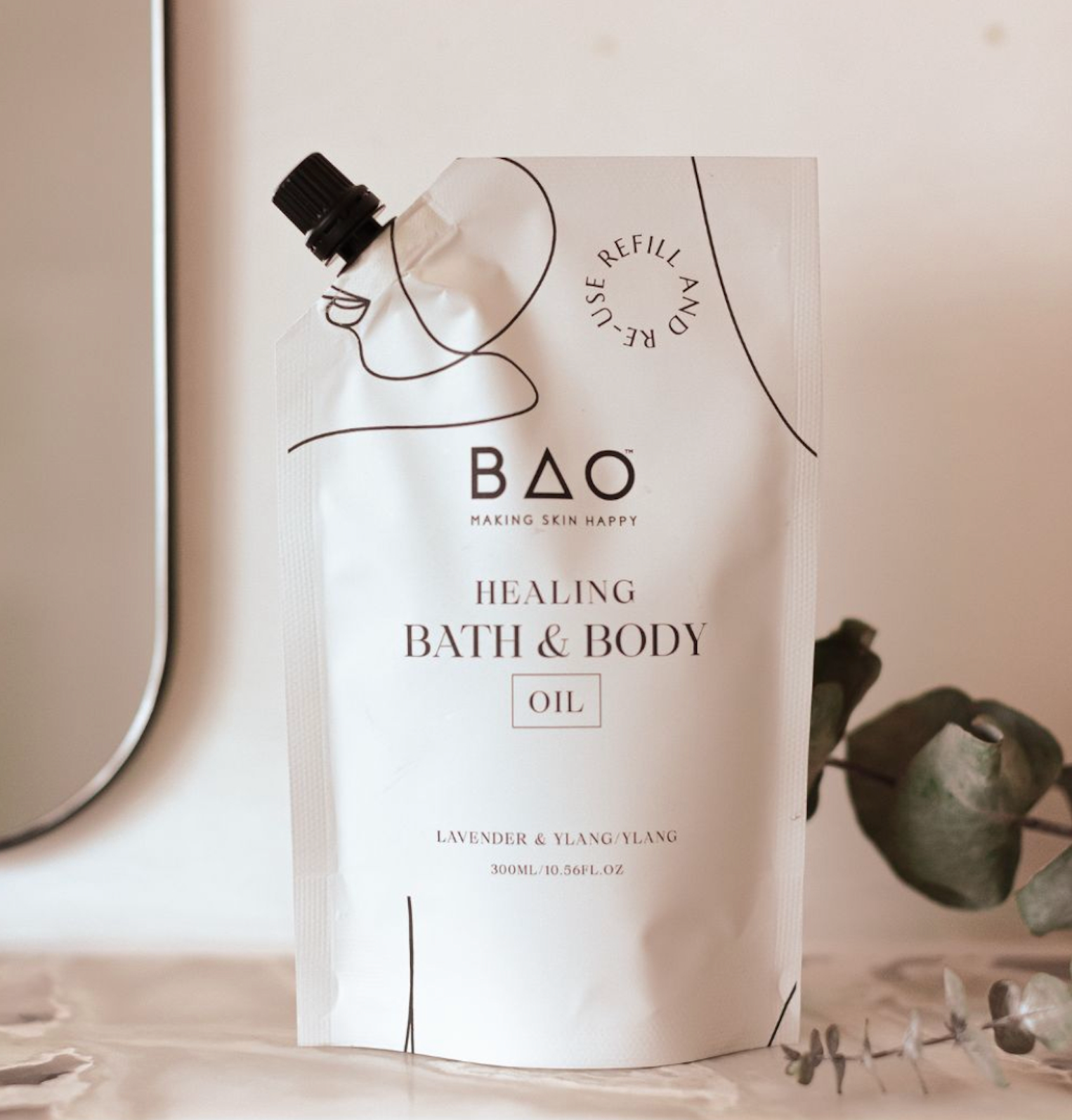 BAO Healing Bath &amp; Body Oil refill pouch standing on a bathroom counter with a eucalyptus sprig