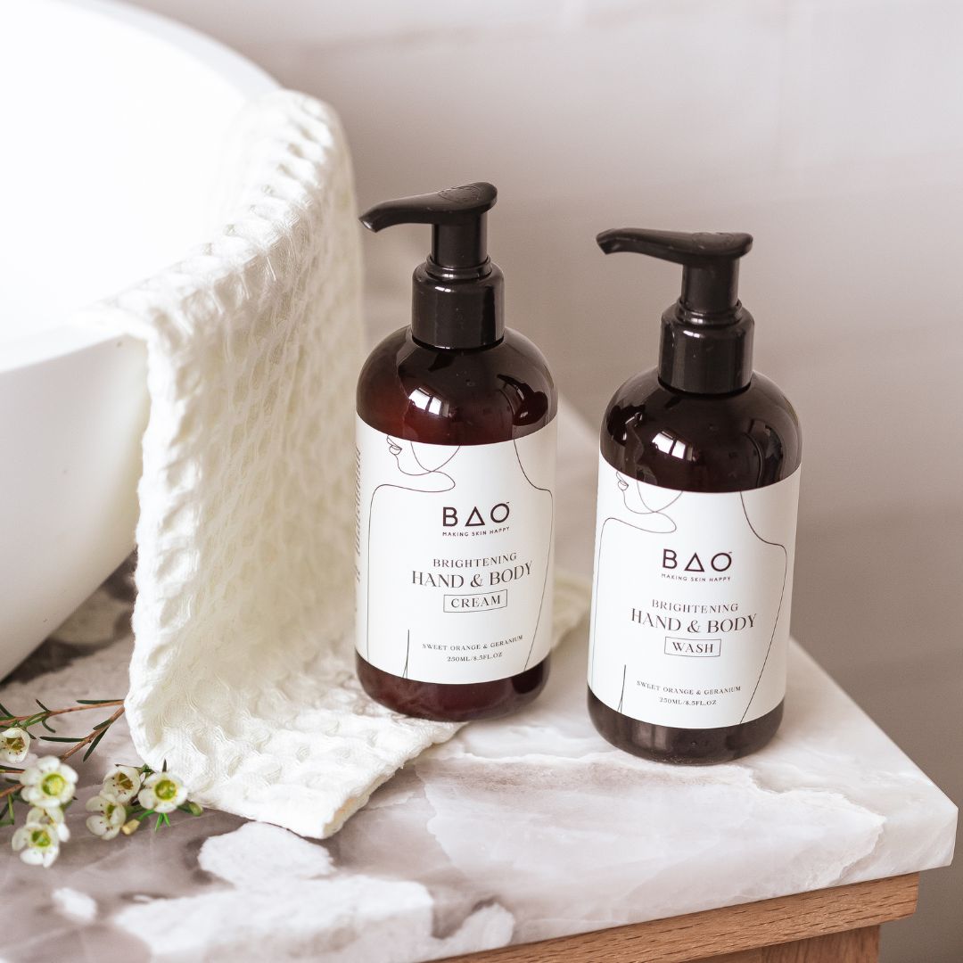 BAO Brightening Hand &amp; Body Wash and Cream bottles beside a folded towel and daisies