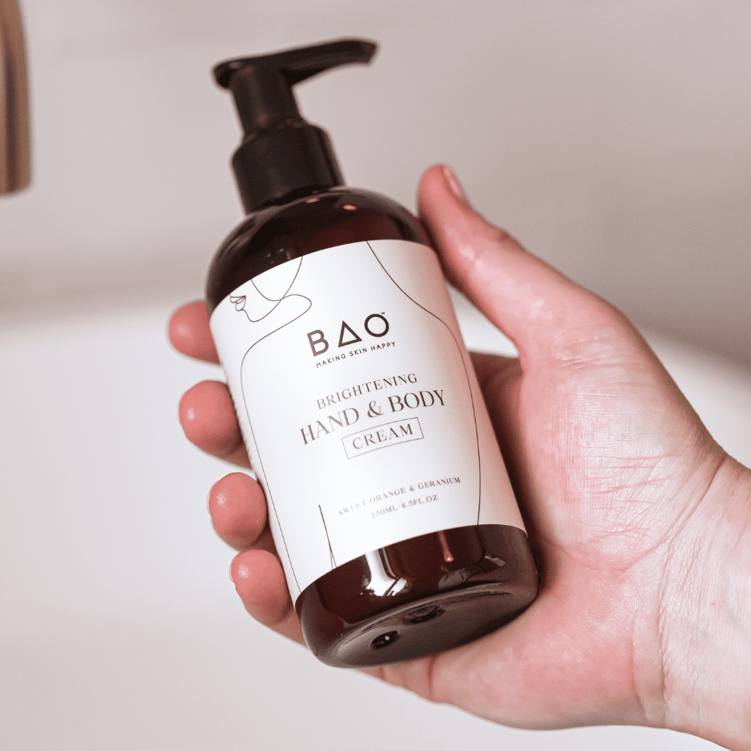 Hand holding BAO Brightening Hand &amp; Body Cream bottle beside a bathroom sink