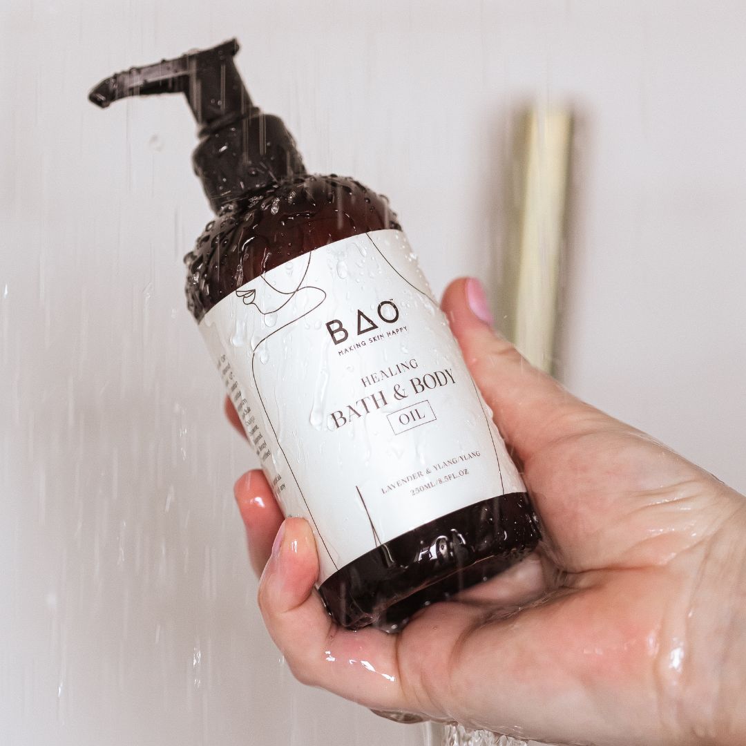 Hand holding BAO Healing Bath &amp; Body Oil bottle under running shower water