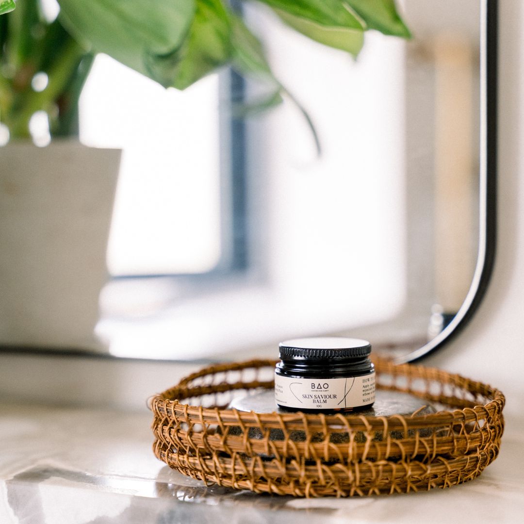 BAO Skin Saviour Balm jar on a mirrored tray beside a bathroom mirror and plant