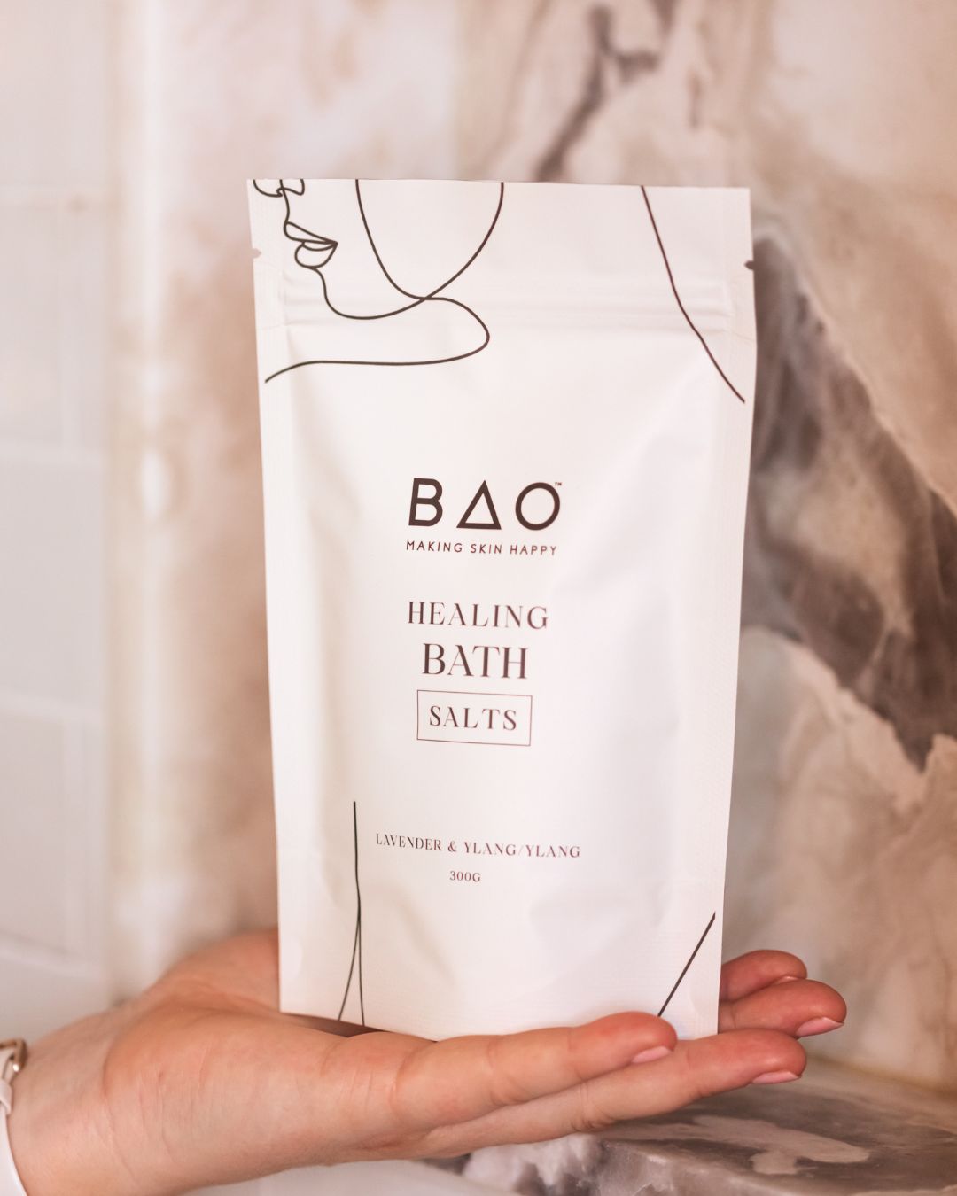 Hand holding BAO Healing Bath Salts pouch against a marble bathroom backdrop