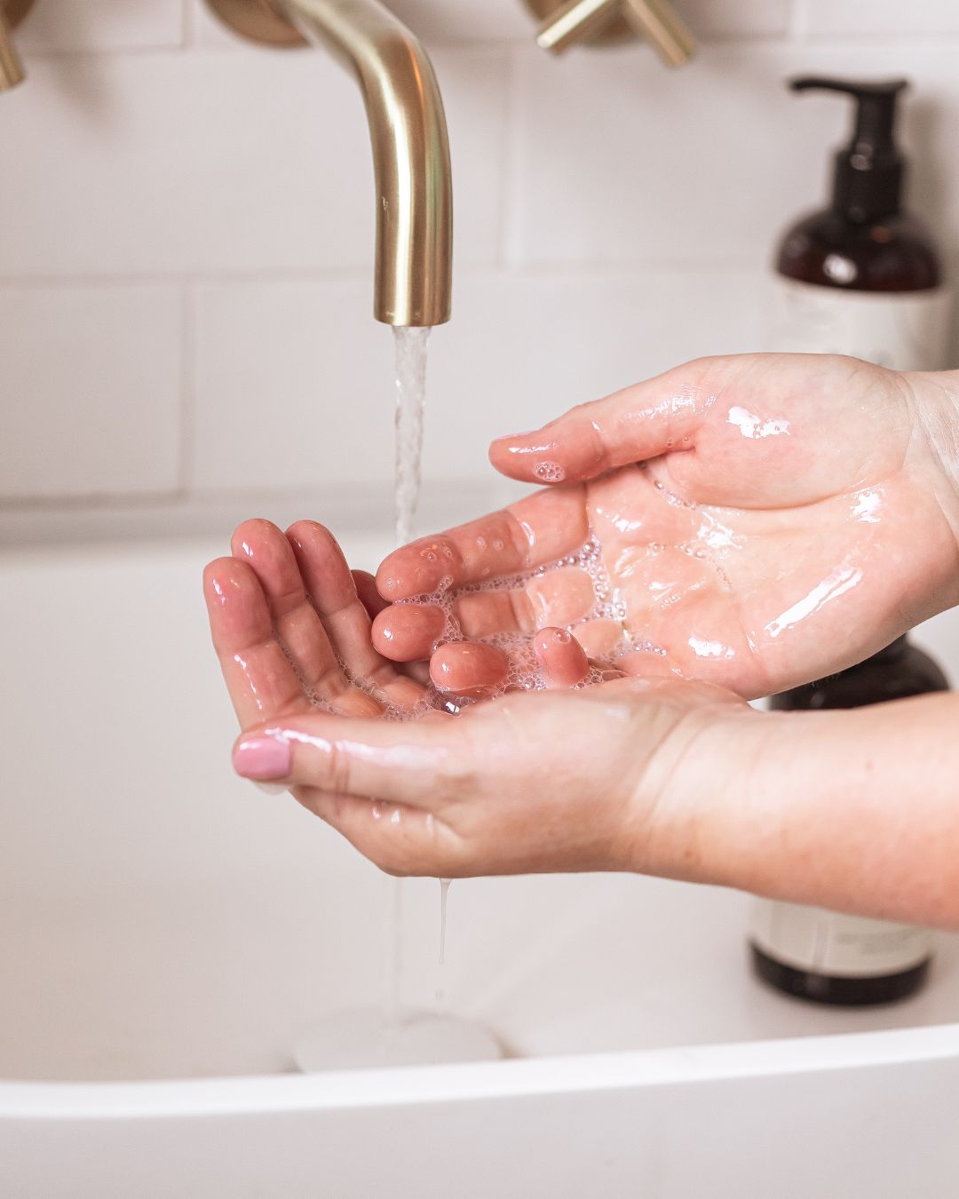 Hands washing under running water with BAO Brightening Hand &amp; Body Wash bottle in the background